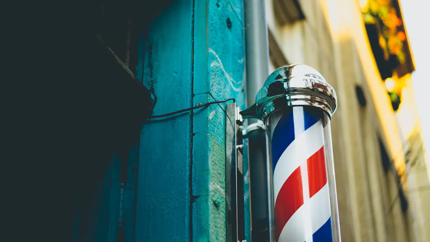 Poste de barbero rojo, blanco y azul en una pared del barrio